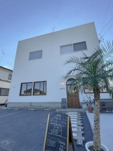 a white building with a palm tree in front of it at Bridge33 CAFE AND HOSTEL in Takagi
