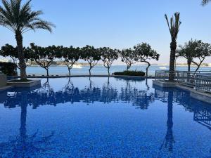 una piscina con palmeras y el océano en Lux Living on Palm Jumeirah With Beach Access & Complimentary Golf, en Dubái