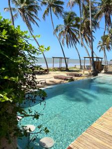 a swimming pool next to a beach with palm trees at Kuarasy Boutique Hotel Japaratinga in Japaratinga