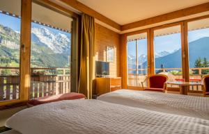 a bedroom with two beds and a balcony with mountains at Hotel Jungfraublick in Wengen