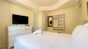 um quarto com uma cama branca e uma televisão de ecrã plano em Pousada Azores Bombinhas em Bombinhas