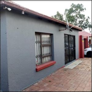 a white building with a red window and gate at Rona Thina House in Pimville