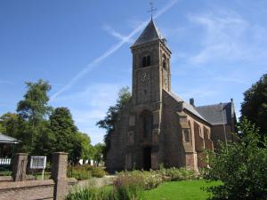 an old church with a tower with a clock on it at Studio Even dur Uut in Noordgouwe