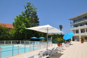 una piscina con sillas y sombrillas junto a un edificio en Appartement Golf et Nivelle avec piscine et parking en Ciboure