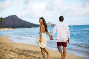 a man and a woman walking on the beach at Hilton Hawaiian Village Waikiki Beach Resort in Honolulu