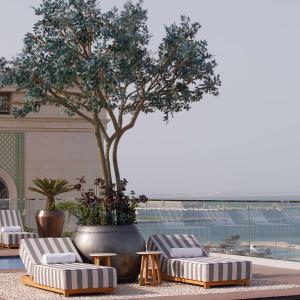 a group of lounge chairs and a tree on a building at The Plaza Doha, LXR Hotels & Resorts in Doha