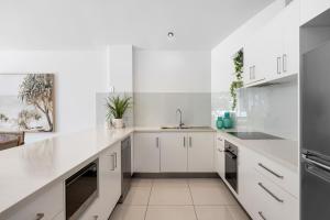 a white kitchen with white cabinets and stainless steel appliances at Noosa Outrigger Beach Resort in Noosaville