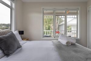 a white bedroom with a large white bed with windows at Derwent River Cottage - Tranquil Waterfront Living in Goodwood