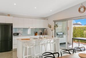 a kitchen with white cabinets and a counter with stools at Zen Garden Beach House Casuarina by uHoliday in Casuarina +6 photos