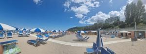 a beach with blue chairs and umbrellas on the sand at Hotel Sans Souci in Gabicce Mare