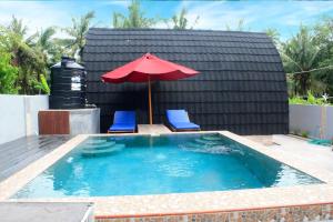 a swimming pool with a red umbrella and two blue chairs and an umbrella at Sekar Kuning Cottage in Toyapakeh