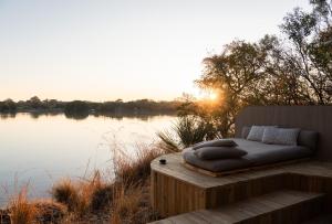 a bed sitting on a deck next to a body of water at Victoria Falls River Lodge in Victoria Falls
