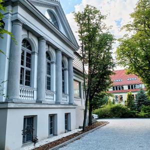 a white building with a tree next to a street at Stare Kasyno Aparthotel in Wrocław