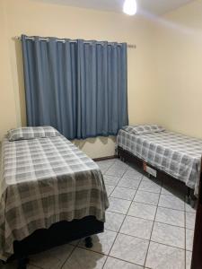 two beds in a room with blue curtains at Solar de Bruna - Apartamento com 2 Qts - 1 Suíte - Garagem coberta - Wi-Fi - Netflix - Acomoda 6 pessoas a 70 metros da praia in Guarapari