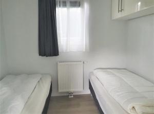 2 camas en una habitación con ventana y radiador en Knus chalet Heidebloem, en Putten