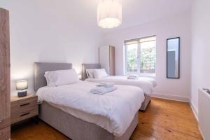 2 camas en un dormitorio con paredes blancas y suelo de madera en Gertrude House - Spacious 3BR Bungalow in Nottingham, en Nottingham