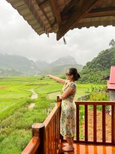 a woman standing on a balcony looking at a field at Đồng Lâm Ecolodge Homestay in Hữu Lũng