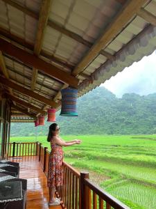 a woman standing on a balcony looking out at a field at Đồng Lâm Ecolodge Homestay in Hữu Lũng