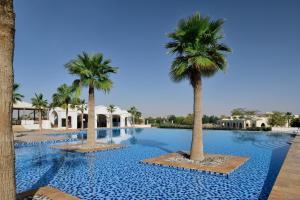 una piscina con palmeras en un complejo en InterContinental Durrat Al Riyadh Resort & Spa, an IHG Hotel, en Riad