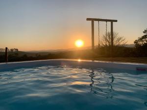 een zwembad met een zonsondergang op de achtergrond bij Recanto Sol Poente in Caçapava