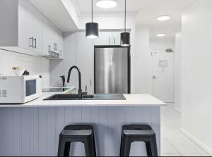 a white kitchen with a sink and two stools at Broadwater Parklands Paradise in Gold Coast