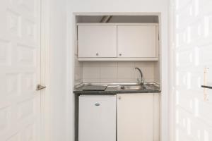 una cocina con armarios blancos y fregadero en Apartamentos Playamaro, en Maro