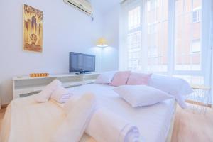 Habitación con cama blanca con almohadas y TV. en For You Rentals Bonito y cómodo estudio cerca al Barrio Tetuán M (ARA1) en Madrid