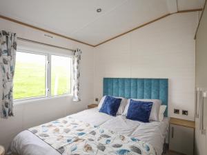 a bedroom with a bed with a blue headboard and a window at Cae'r Wylan in Pwllheli