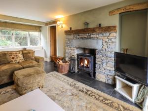 a living room with a stone fireplace and a television at Foxdene Cottage in Underbarrow