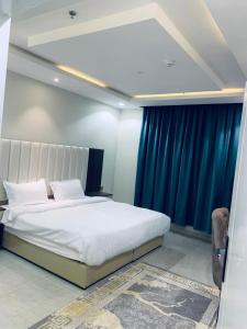 a bedroom with a large white bed with blue curtains at أزهار النرجس للشقق الفندقية in Umm al Khashab