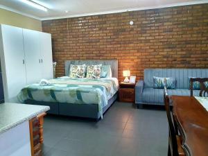 um quarto com uma cama, um sofá e uma parede de tijolos em Garden cottages near Savannah Mall em Polokwane