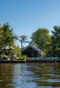 a man sitting on a dock next to a house on the water at Pean-buiten Waterlodges in Nes