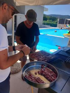 two men preparing food on a grill next to a pool at Giannis Villa in Skinés