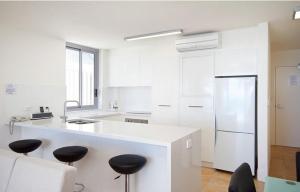 a white kitchen with white appliances and black stools at Fairshore Apartment 28, Noosa Heads in Noosa Heads