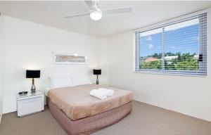 a white bedroom with a bed and a window at Fairshore 28 Beachfront Escape in Noosa Heads
