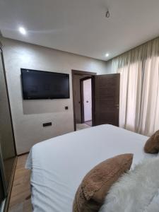 een slaapkamer met een wit bed en een flatscreen-tv bij L3 avec piscine in Agadir