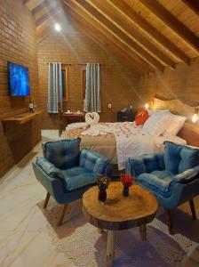 een slaapkamer met een bed en blauwe stoelen en een tafel bij Pousada das Castanheiras in Monte Verde