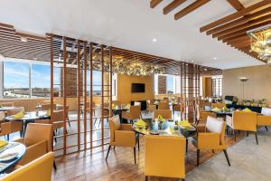 un restaurante con sillas amarillas, mesas y ventanas en V Hotel Dubai, Curio Collection by Hilton, en Dubái