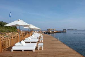 Susona Bodrum, LXR Hotels & Resorts في بودروم: صف من كراسي الصالة البيضاء على رصيف مع الماء