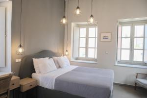 a bedroom with a bed with white sheets and two windows at Metochi Athentic Hospitality in Hydra