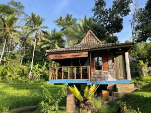 a small house in a field with palm trees at Oemah Tepi Sawah in Jatiluwih