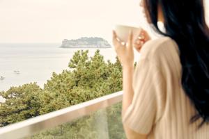a woman holding a cup of coffee looking at the ocean at JW Marriott Jeju Resort & Spa in Seogwipo