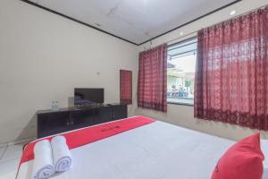 een slaapkamer met een bed met rode gordijnen en een raam bij RedDoorz Syariah near Taman Kota Kuningan in Kuningan