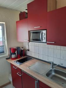 uma cozinha com armários vermelhos, um lavatório e um micro-ondas em Gästehaus Labahn em Ückeritz