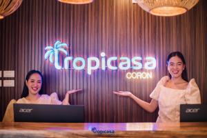 コロンにあるTropicasa Coron Resort & Hotelの看板の裏に立つ二人