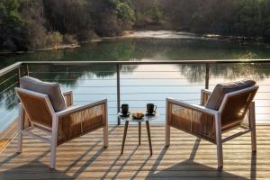 two chairs and a table on a deck next to a lake at Riverhorse Lodge in Lanseria