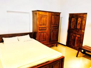 a bedroom with a bed and a wooden cabinet at Thanamal-villa in Tanamalwila