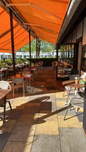 an outdoor patio with tables and chairs and orange umbrellas at Hotel und Restaurant Zeus in Wolfsburg