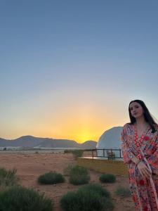a woman standing in the desert with the sunset in the background at Bubble camp 2 in Wadi Rum