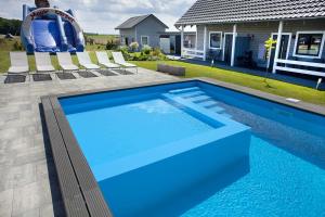 una piscina azul con sillas y frente a una casa en U Ani Domki z podgrzewanym basenem, en Rewal